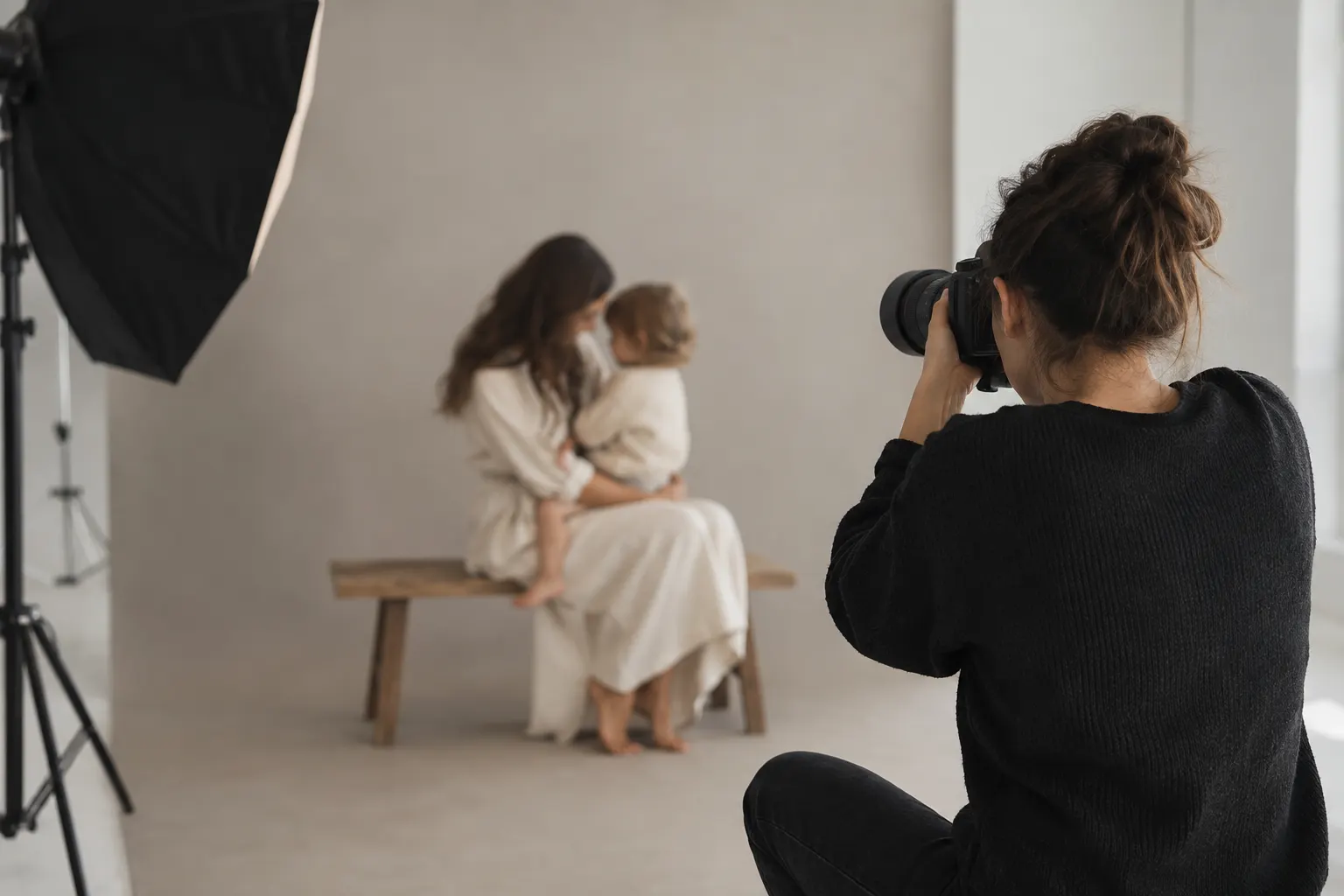 Fotógrafa en una sesión de fotos de una madre con su hijo en un estudio con fondo claro y softbox